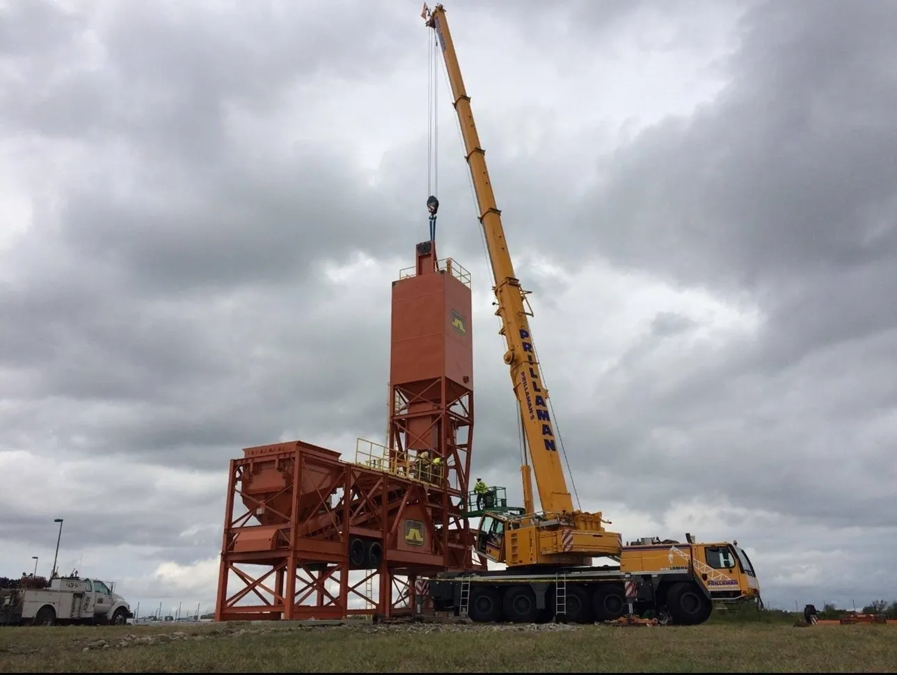 A crane is lifting a cement mixer into the ground.