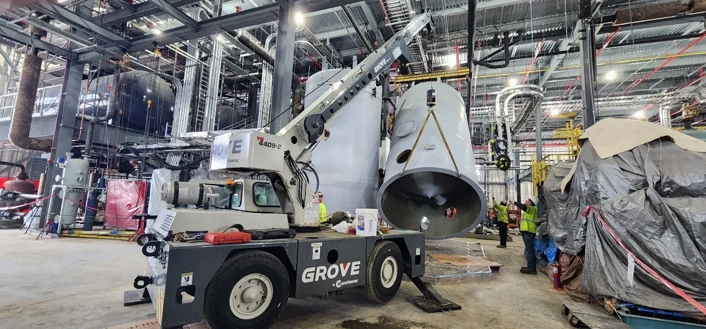 A crane is lifting a large metal cylinder.