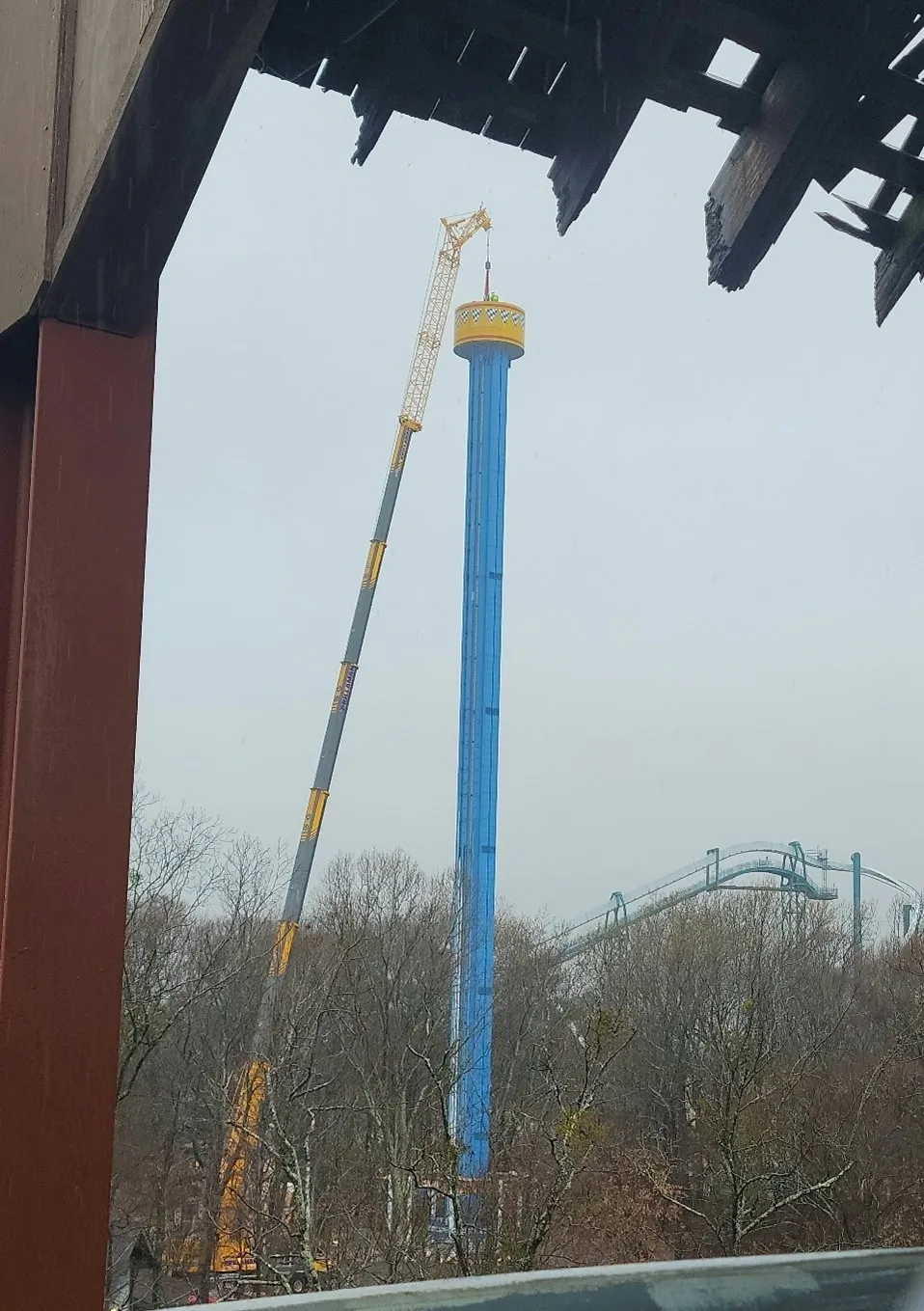 A blue and yellow roller coaster with two cranes on top of it.