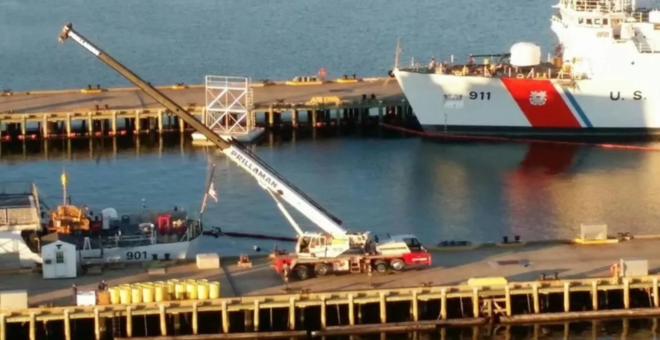 A crane is in the foreground with a large ship in the background.