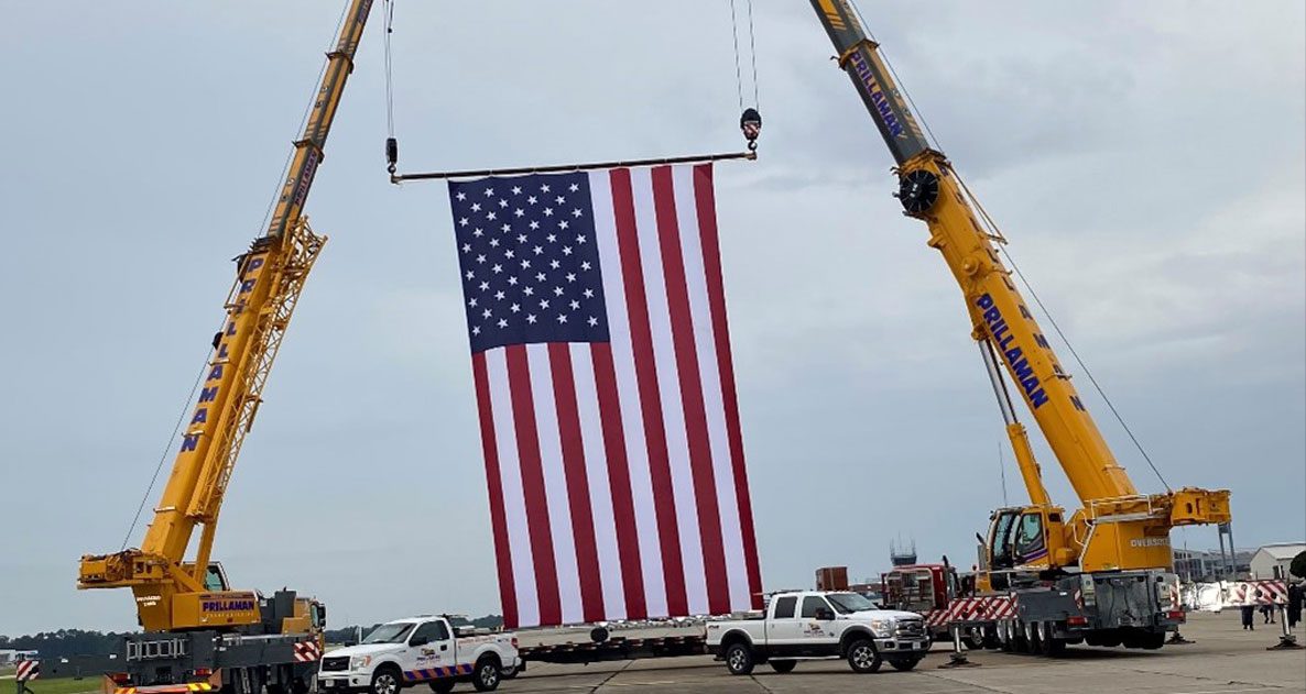 A large american flag being lifted by cranes.